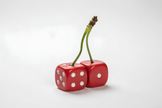 Two red dice shaped cherries with green stems against a bright studio light conveying chance