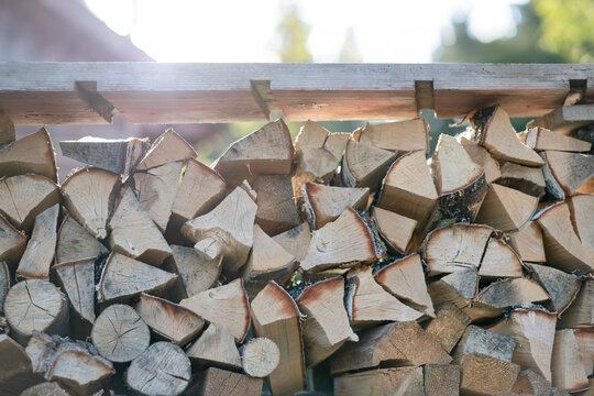 Stack of split firewood neatly stored on a wooden rack outdoors, illuminated by warm natural sunlight.