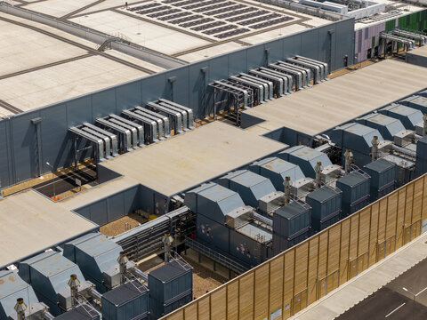 Aerial view of a modern data center facility featuring large industrial cooling units, ventilation systems, and flat rooftops in the United Kingdom.