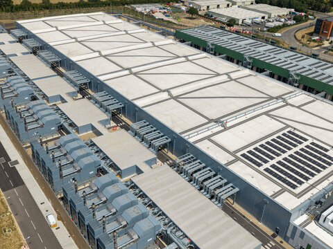 Aerial view of a large data center facility featuring extensive rooftop HVAC units and solar panel arrays in an industrial area in the United Kingdom.