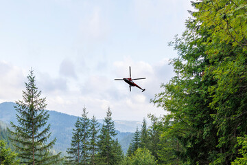 Fototapeta premium Rescue Helicopter Flying Over Green Mountain Forest Landscape