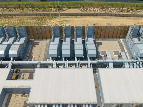 Aerial view of a data center facility featuring rows of industrial cooling units and power infrastructure on a flat roof, surrounded by a perimeter fence in the United Kingdom.