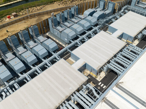 Aerial view of a data center featuring rows of industrial cooling units and HVAC infrastructure on the roof, with metal piping and a perimeter fence in the United Kingdom.