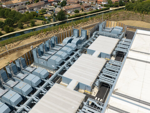 Aerial view of a modern data center facility featuring rows of industrial cooling units and complex mechanical infrastructure situated near a canal in the United Kingdom.