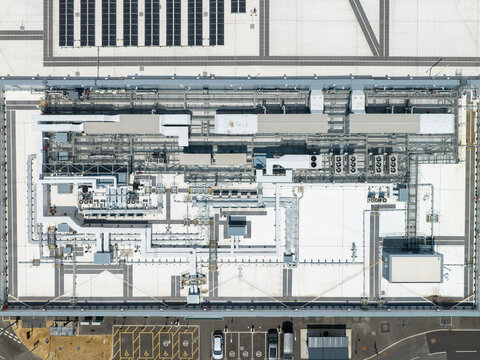 Aerial view of a data center roof featuring complex HVAC systems, ventilation units, and industrial piping, with a parking area visible at the bottom in United Kingdom.
