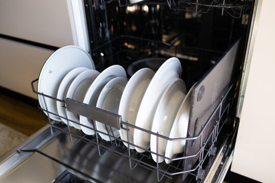 Close-up of an open modern built-in dishwasher packed with plates, mugs, and cutlery. Domestic chores, home appliance, and kitchen interior concept with selective focus.