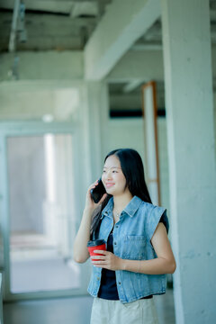 Young Asian woman reading a book with headphones and laptop by the window