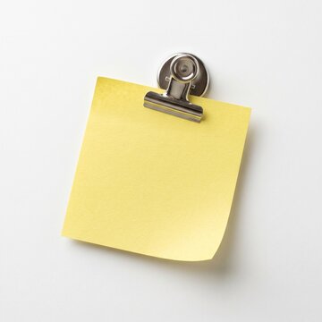 Blank yellow sticky note held by a metallic clip on a clean white background, ideal for custom notes, reminders, and copy space.