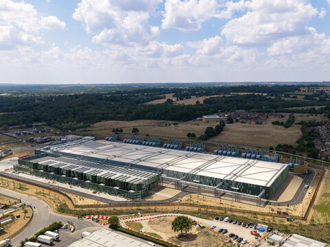 Aerial view of a large data center facility with industrial architecture, surrounding green fields, and access roads in the United Kingdom.