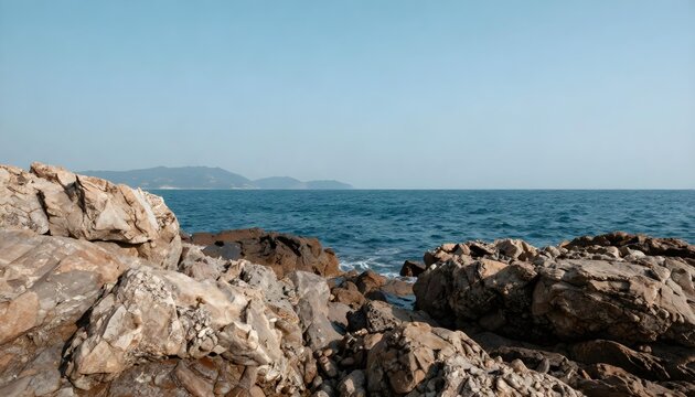 Serene seascape with rugged rocks and distant hazy mountains under a clear sky