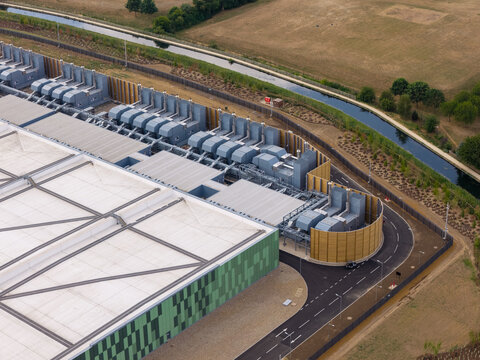 Aerial view of a modern data center featuring a large green patterned facade and extensive rooftop cooling infrastructure situated next to a canal in the United Kingdom.