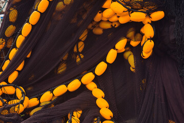 Close-up of black fishing nets piled together with bright yellow flotation buoys attached to the ropes. The contrasting colors and intricate mesh create an abstract maritime texture © EvaMara