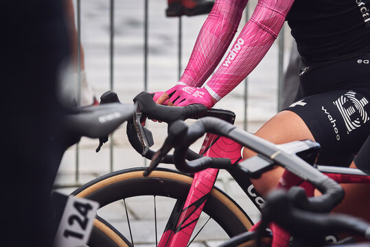 Close-up of a female road cyclist wearing pink Wahoo-branded sleeves and gloves, black cycling shorts with the Wahoo logo and a colorful EF Education cycling team emblem. 
