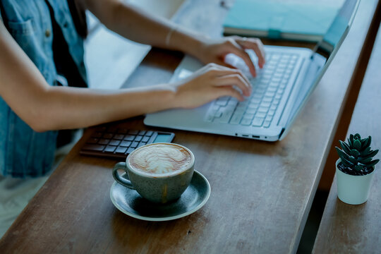 Hand using smartphone while working on laptop with coffee in modern workspace