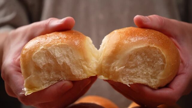 Close-up of two fresh, soft, golden-brown yeast buns being torn in half; slow motion.