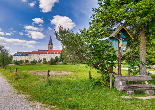 Wegkreuz und Bank dahinter die Erzabtei Sankt Ottilien, Kloster der Missionsbenediktiner, Eresing, Bayern, Deuschland