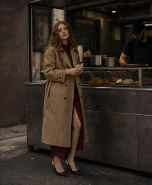 Stylish woman eating street food. Trendy girl holding snack at outdoor food stall.