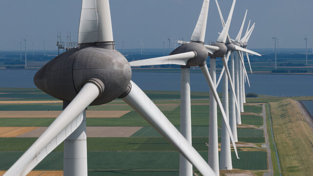 Aerial view of a row of wind turbines standing in agricultural fields near the coast in Nagele, Flevoland, Netherlands.