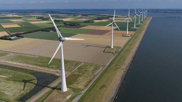 Aerial view of a row of modern wind turbines standing along a dike next to agricultural fields in Nagele, Flevoland, Netherlands.