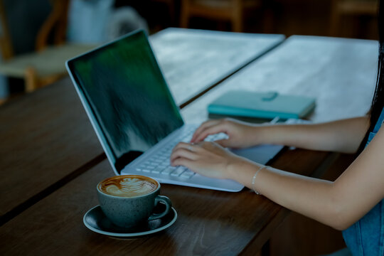 Hand using smartphone while working on laptop with coffee in modern workspace