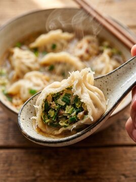 Steamed dumpling in ceramic spoon. Asian vegetable gyoza served in hot broth bowl.
