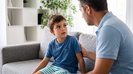 Fototapeta premium Caring father providing emotional support to young son sitting on living room