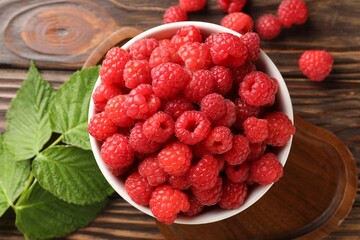 Tasty ripe raspberries in bowl and leaves on wooden table, flat lay © New Africa