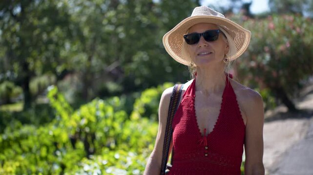 A senior woman happily explores a winery in Napa, soaking in the sun and stunning vineyard views while enjoying her winery tour.