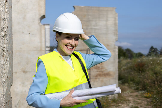 Woman architect engineer smiling carrying blueprints on construction site