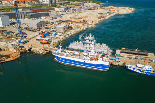 Aerial view of a shipyard in Tromso with a blue fishing vessel docked at the pier after completion, featuring industrial buildings and calm fjord waters in Tromso, Troms, Norway.