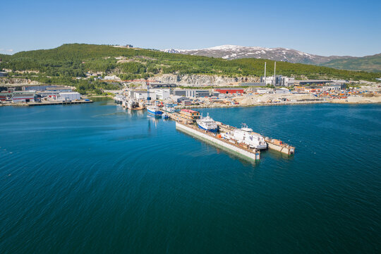 Aerial view of a shipyard in Tromso with ships docked in a dry dock, industrial facilities, and snow-capped mountains in the background, Tromso, Troms, Norway.