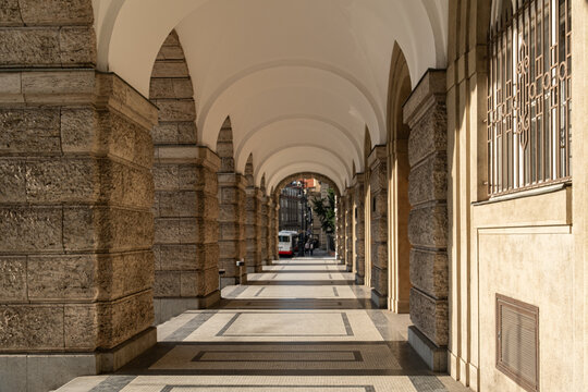 perspective view through a covered stone colonnade Arcade with vaulted white ceilings and massive rusticated stone pillars along a street in Prague