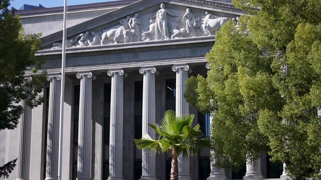 Building features detailed design and statues under clear sky while green trees provide shade near California State Capitol