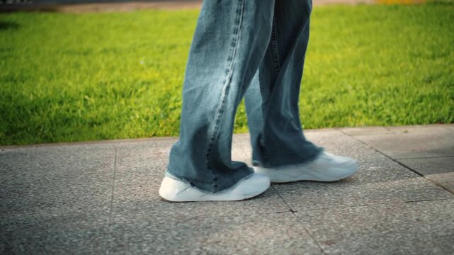 Side close-up of an anonymous woman's feet walking on a street with grass in the background, showing movement, nature, and outdoor lifestyle.
