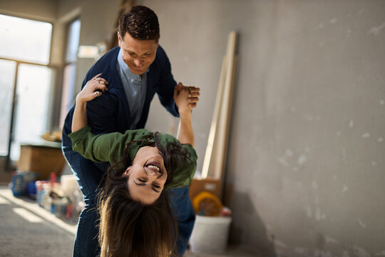 A happy young couple smiling and dancing inside an unfinished room during a cooperative home improvement project.