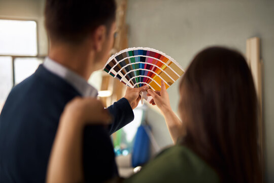 Couple cooperating and selecting wall paint colors inside an unfinished room during a home renovation project. Focus is on color swatch.