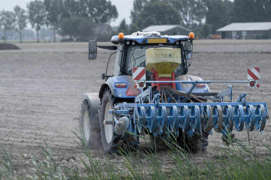 Rear view of  Blue Tractor Working on Dry Dusty Farmland