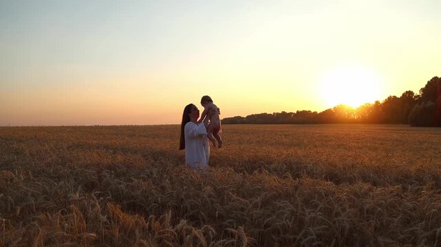A happy mother and her seven-month-old son spin in a wheat field in the rays of the setting sun