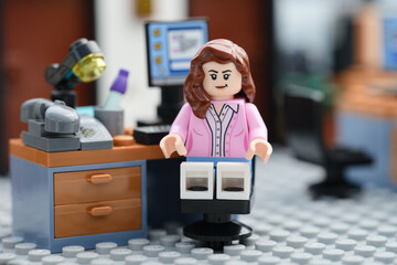 Fototapeta premium Tambov, Russian Federation - July 30, 2026 A happy Lego businesswoman minifigure sitting on a chair behind a computer in an office and looking at the camera. Close up.