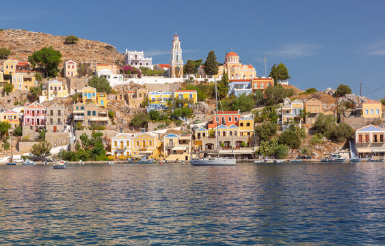 View of the waterfront with the historic clock tower and colorful hillside houses in Symi Harbor, Dodecanese, Greece.