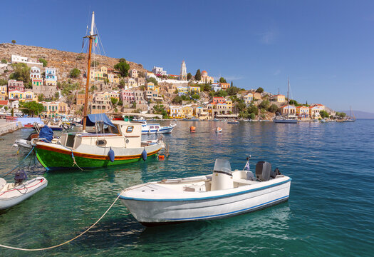 Small boats moored in Symi Harbor with colorful hillside houses and the waterfront of Symi Island, Dodecanese, Greece.