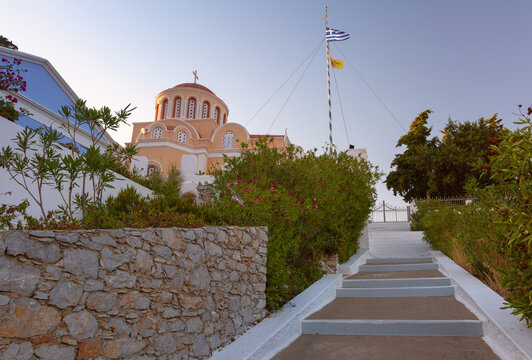 View of a Greek Orthodox church with a dome, stone walls, garden, and staircase on Symi Island, Dodecanese, Greece.