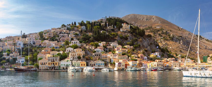 Panoramic view of Symi Harbor with colorful neoclassical houses, yachts, and rocky hills on Symi Island, Dodecanese, Greece.