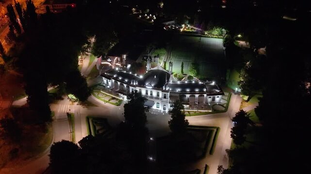 Night aerial footage of the illuminated Korčuliarsky pavil&oacute;n in Ko&scaron;ice, Slovakia. The drone shot reveals the historic architecture, surrounding gardens, pathways and nearby tennis courts.