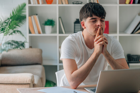 student at their home desk with a laptop, working or studying remotely in an online course, with a thoughtful expression, indicating decision or doubt