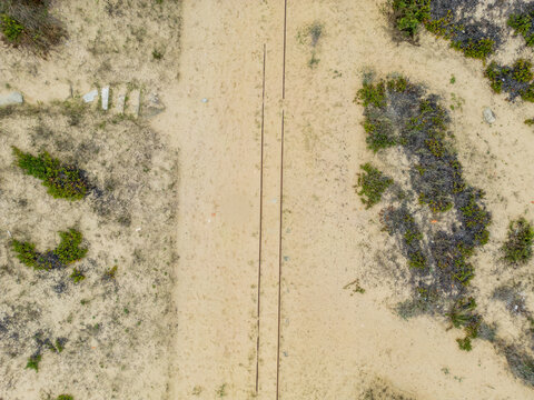 Aerial view of Praia da Mata featuring a sandy path with old tracks running through coastal dunes and sparse vegetation in Costa de Caparica, Setubal, Portugal.