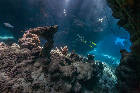 Beautiful coral reef cave with scuba diver and sun rays underwater