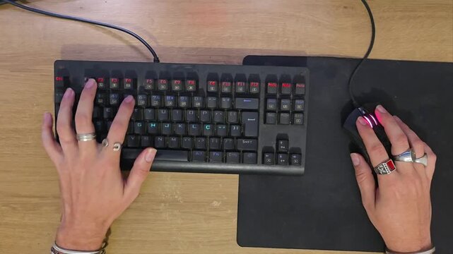 Top-down view of gamer hands typing on mechanical keyboard and clicking mouse during PC gameplay