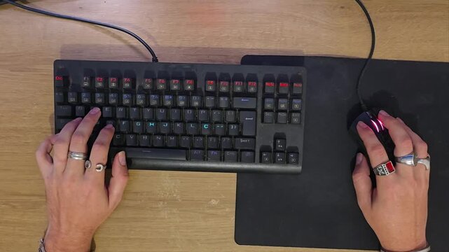 Top-down view of gamer hands typing on mechanical keyboard and clicking mouse during PC gameplay