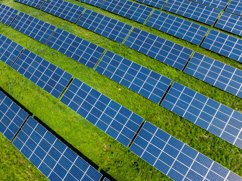 Aerial view of a solar photovoltaic power plant with rows of blue solar panels arranged in neat diagonal lines over a lush green grassy field in Sudbury, Massachusetts, USA.